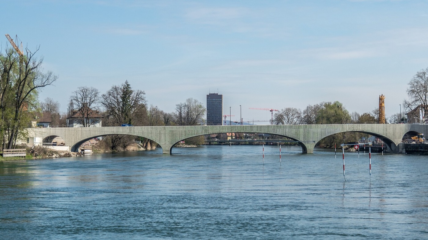 Die heutige Aarebrücke in Aarau: eine flache Betonbogenbrücke mit mehreren Bögen über die breite Aare, im Hintergrund ein Hochhaus und Baukrane